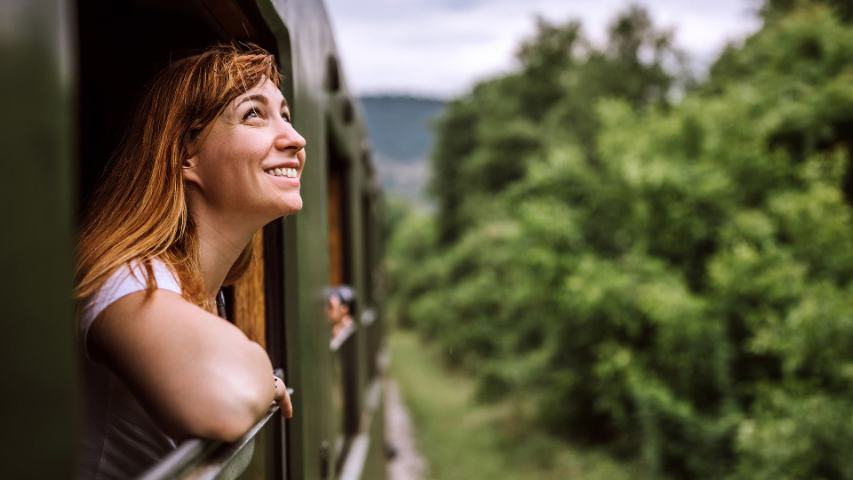 a happy woman leaning out the window of a train as it moves through the countryside